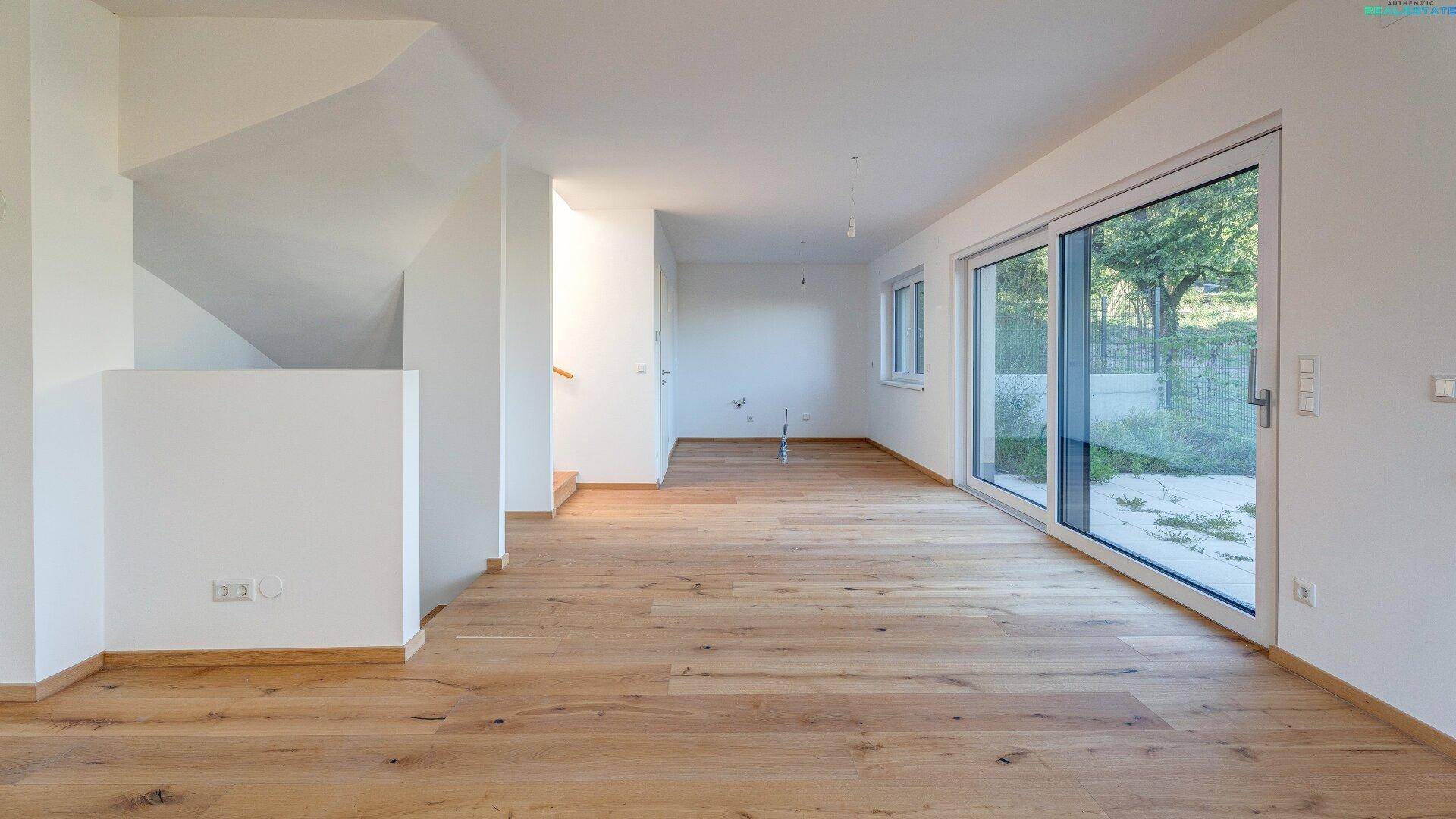 Helles Wohnzimmer mit Holzboden, großen Schiebetüren und Blick ins Grüne, modern und offen gestaltet.
