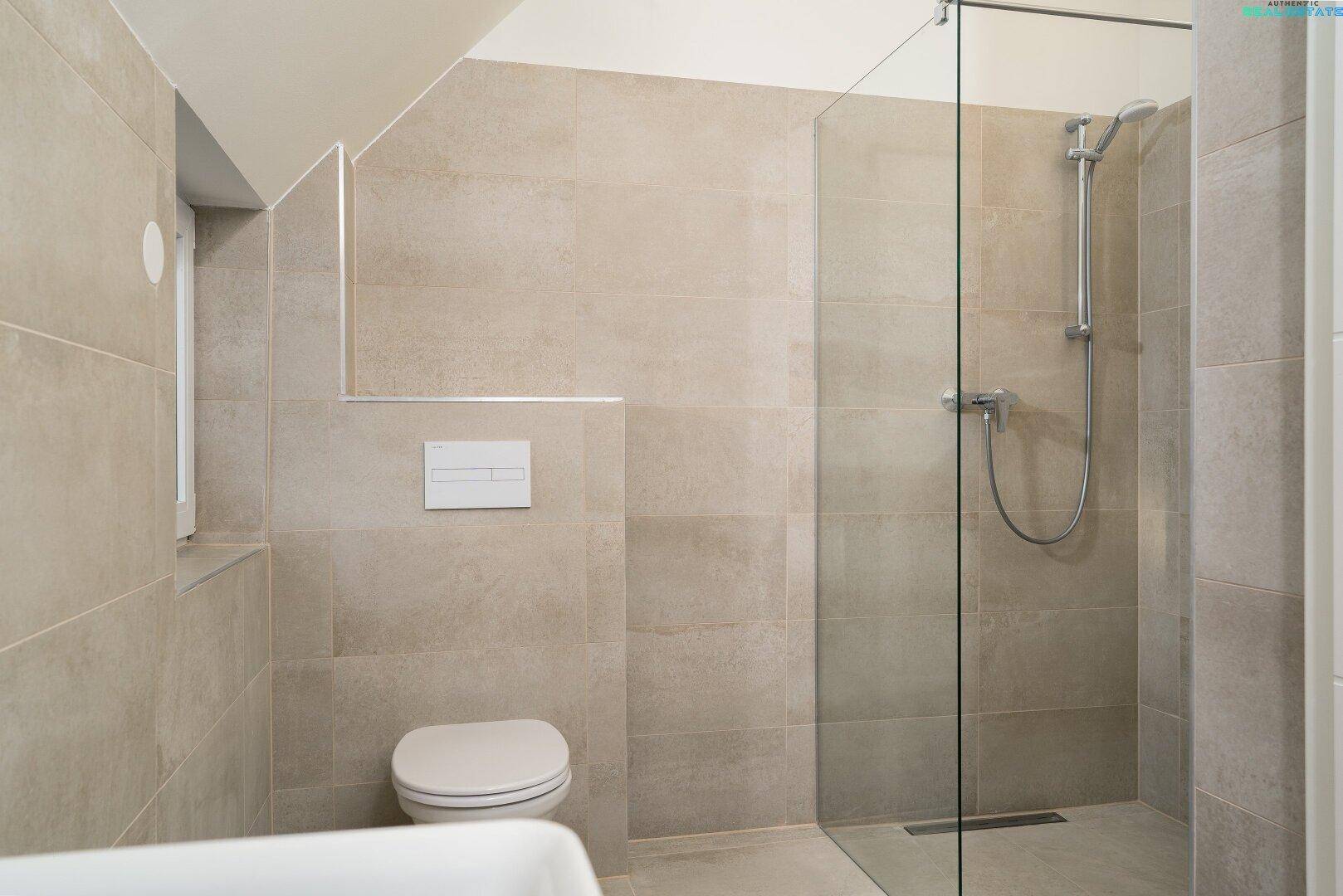 Modernes Badezimmer mit begehbarer Dusche, Wand-WC und hellen Fliesen unter einer Dachschräge.