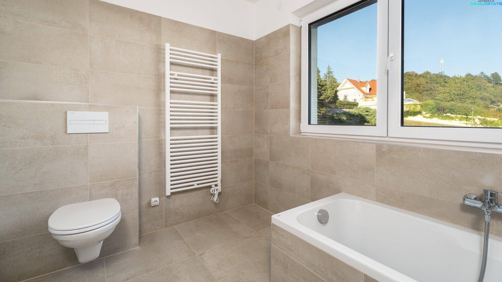 Modernes Badezimmer mit Wand-WC, Badewanne, Handtuchheizkörper und Fenster.