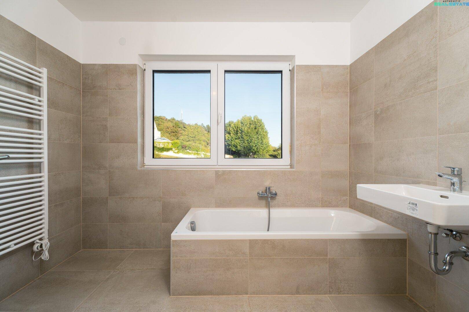 Modernes Badezimmer mit Badewanne, Waschbecken, Handtuchheizkörper und Fenster.