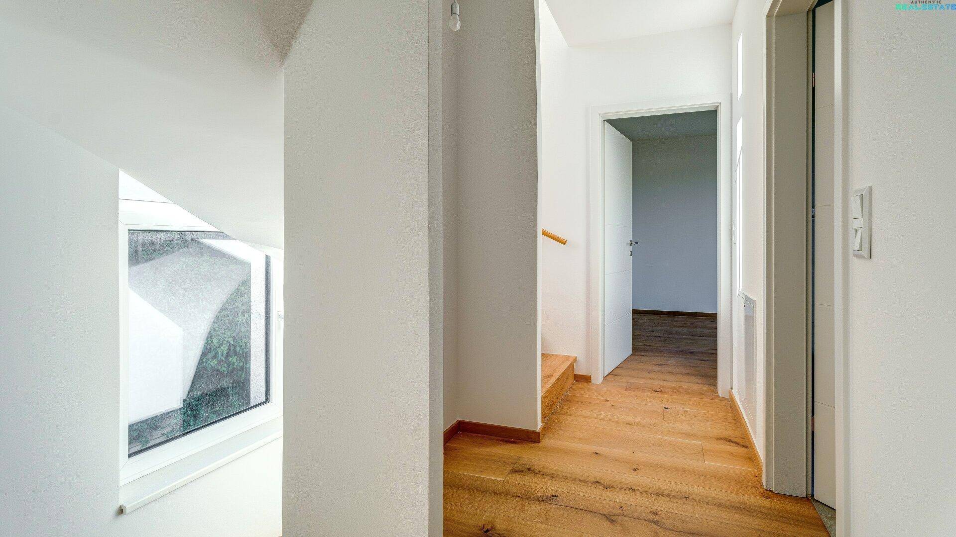 Heller Flur im Obergeschoss mit Holzboden und Treppenaufgang, bietet Zugang zu den Zimmern.