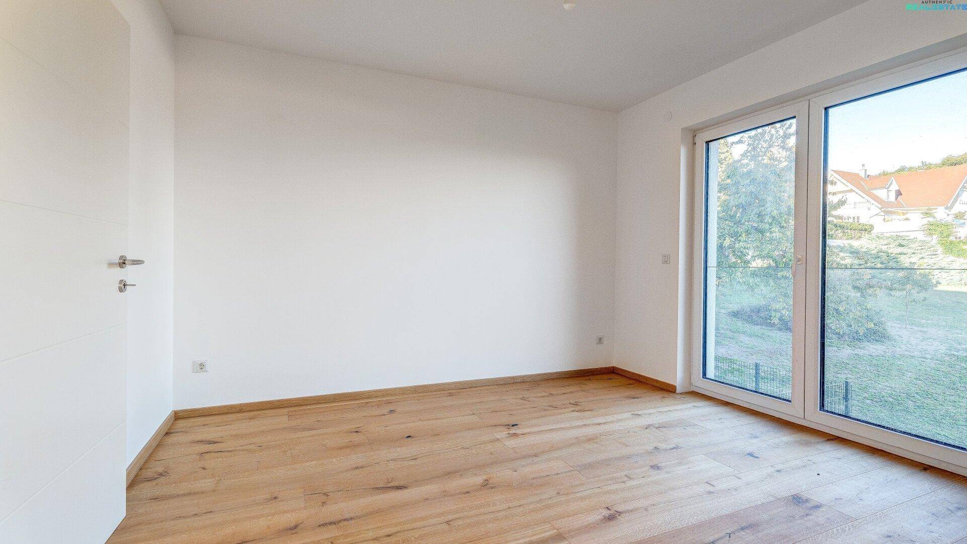 Geräumiges Zimmer mit Holzboden und großen Fenstern, bietet viel Tageslicht und Ausblick.