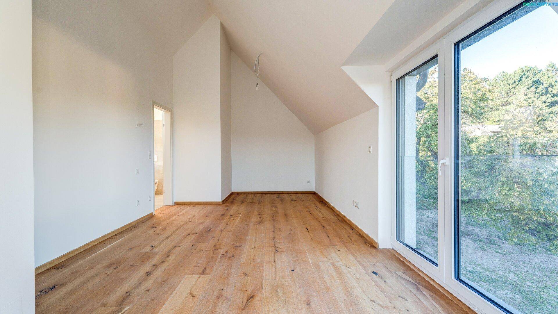 Helles Zimmer mit Holzboden, großen Fenstern und Zugang zum Außenbereich mit Grünblick.