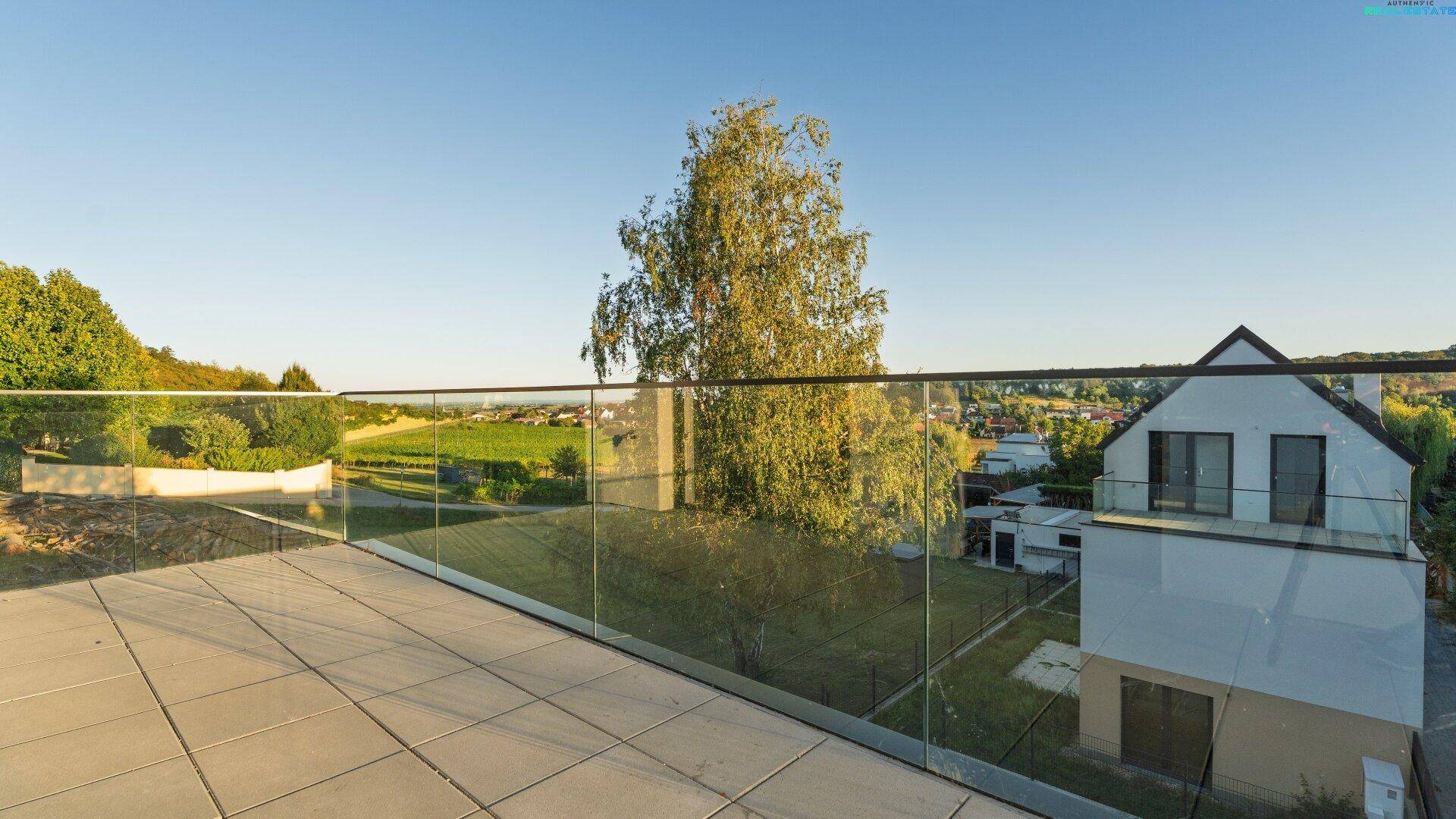 Geräumige Dachterrasse mit modernem Glasgeländer und Panoramablick auf die grüne Umgebung.