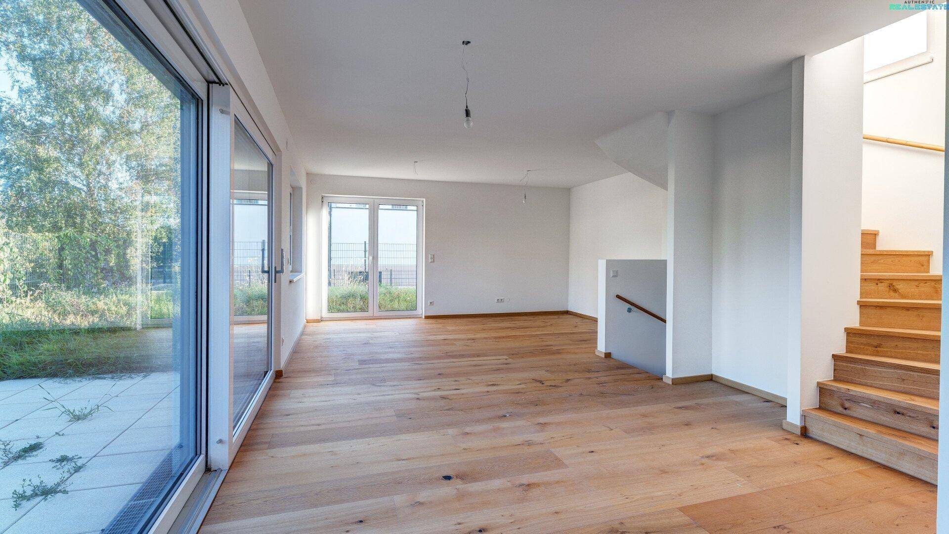 Offener Wohnbereich mit großen Schiebetüren zum Garten und Holztreppe zum Obergeschoss.