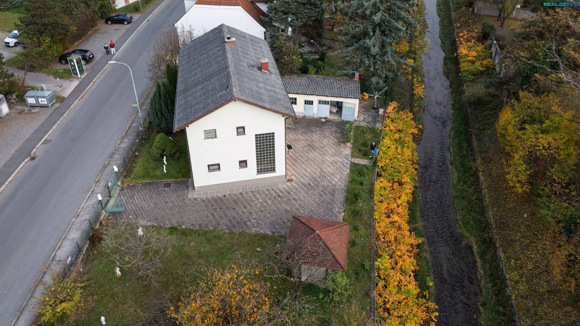 Luftaufnahme des Hauses mit großem Grundstück, Garten und angrenzendem Grünbereich und Bach.