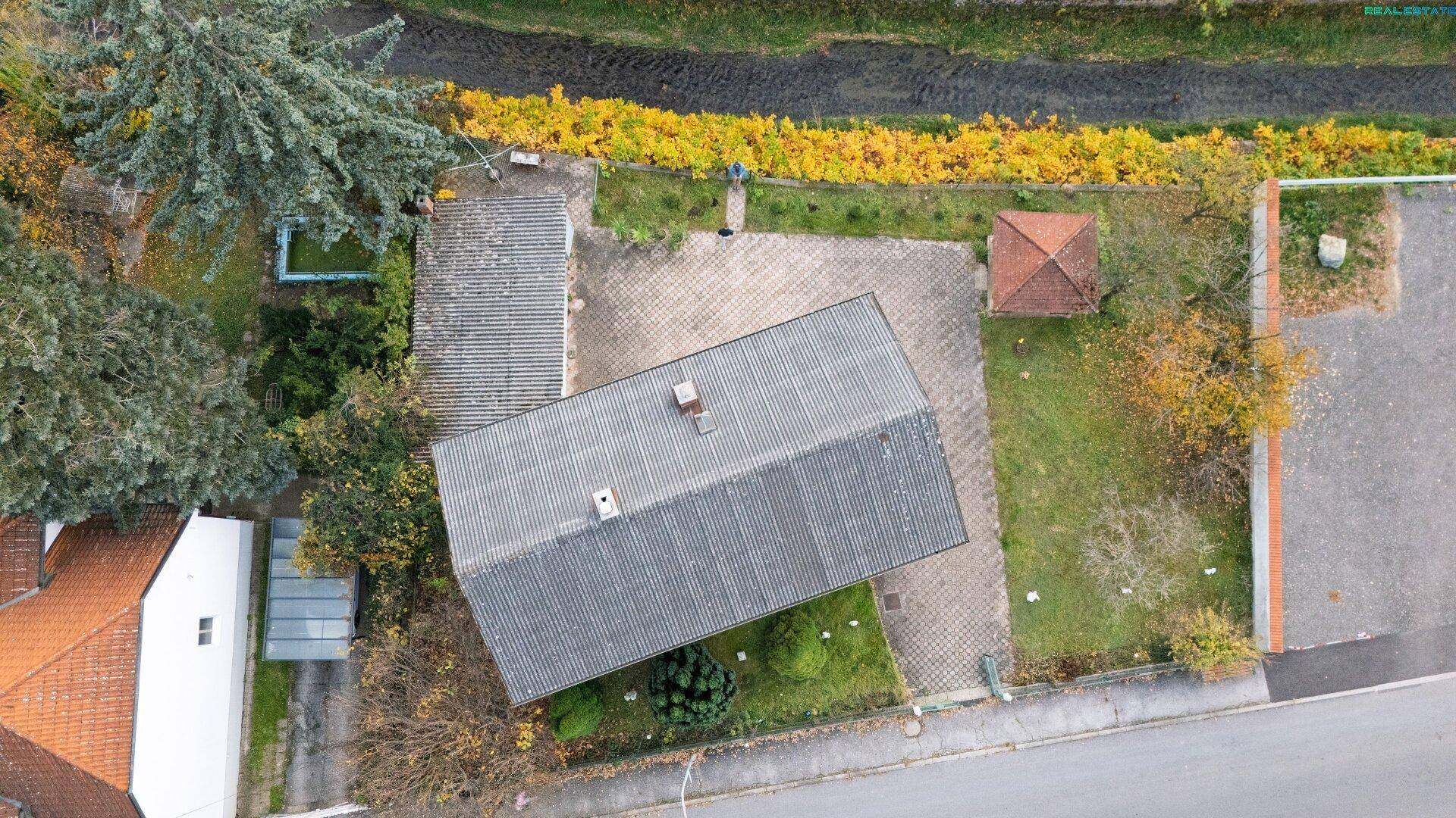 Draufsicht auf das Grundstück mit Haus, Garage, Garten und einem angrenzenden Wasserlauf.