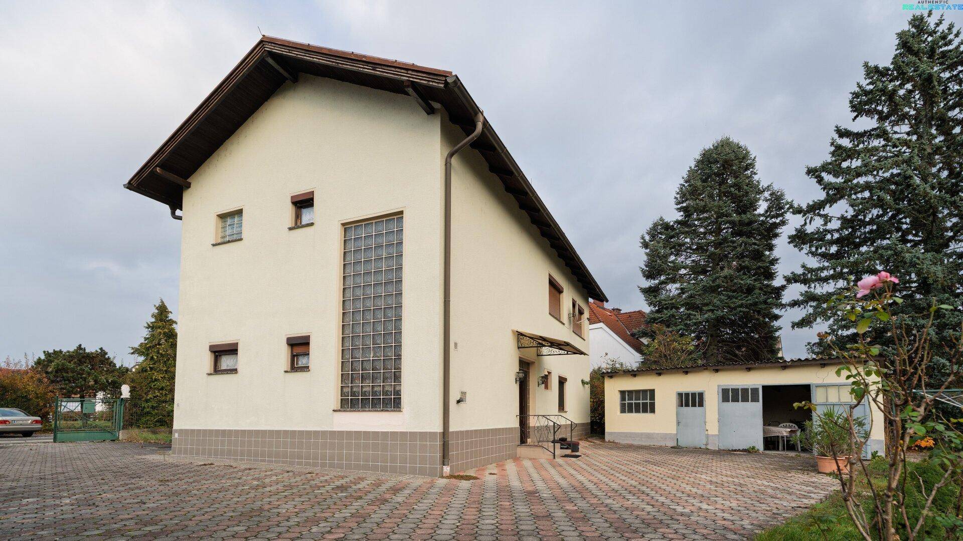 Außenansicht des Hauses mit einer gepflasterten Auffahrt und einer separaten Garage im Hintergrund.
