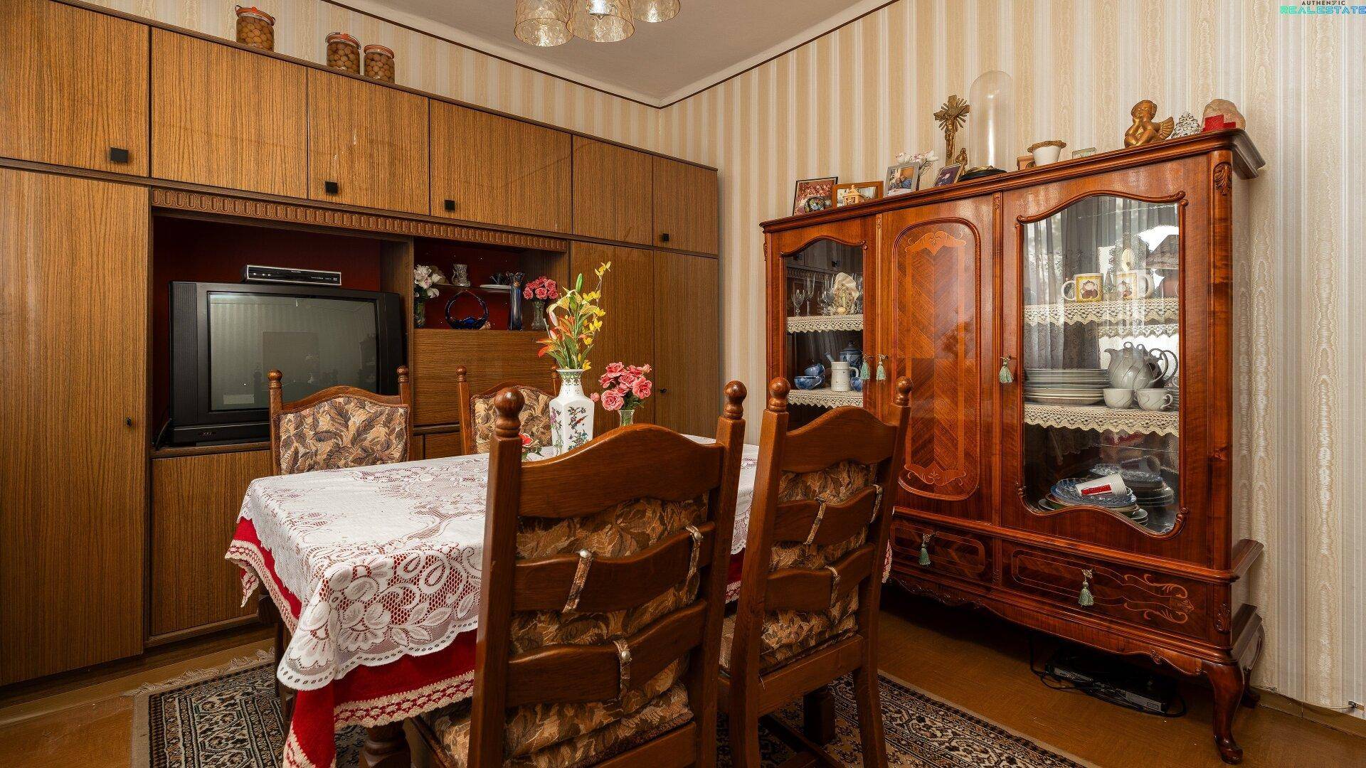 Essbereich mit traditionellen Holzmöbeln, einem großen Vitrinenschrank und gemusterten Tapeten.