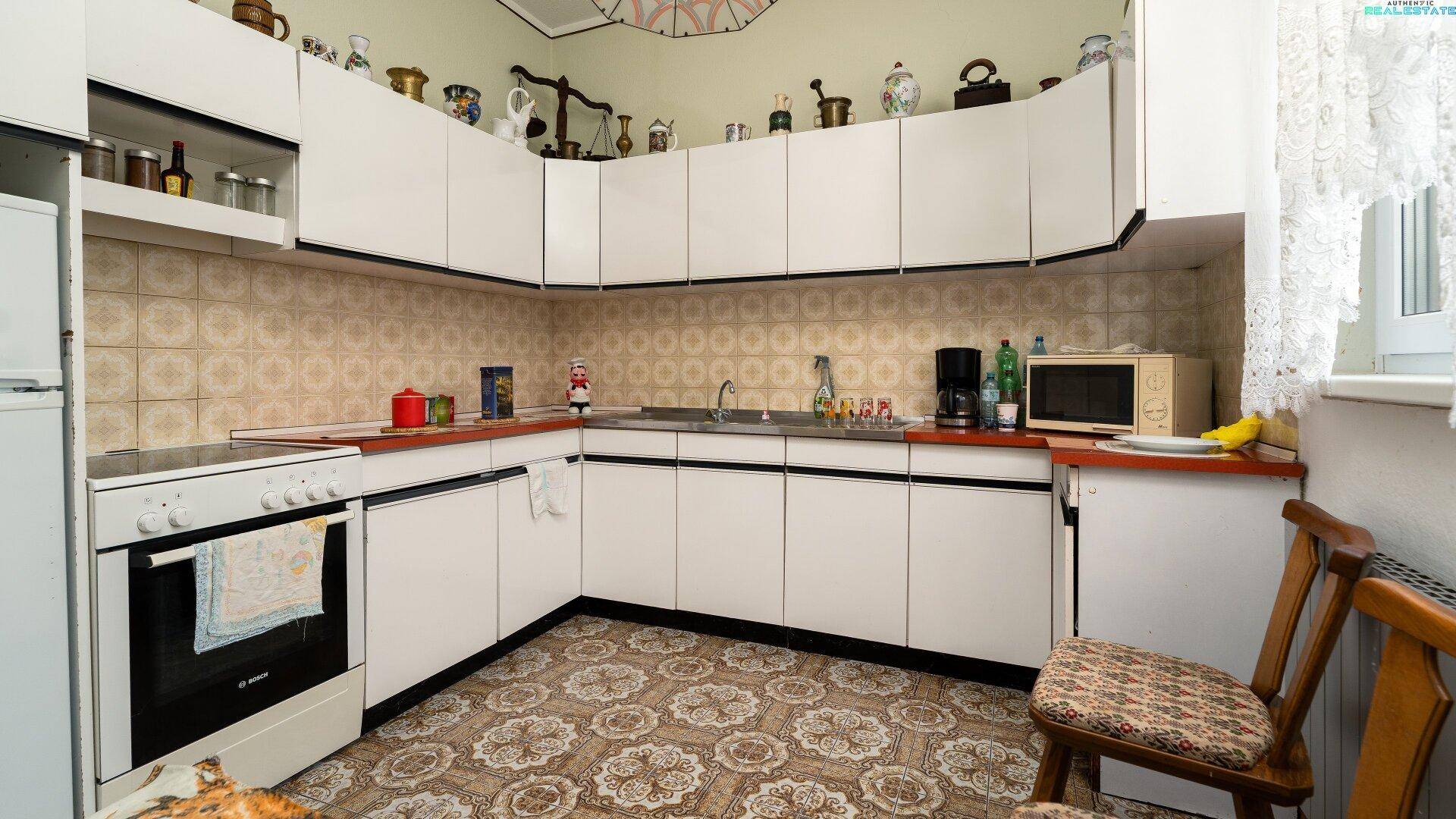 Küche mit weißen Schränken, älteren Fliesen und einem freistehenden Elektroherd mit Backofen.