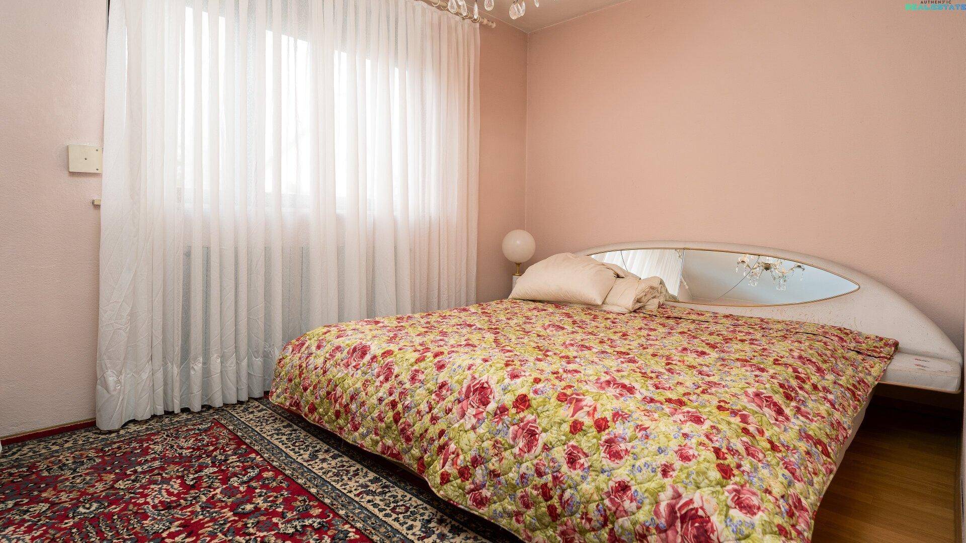 Schlafzimmer mit einer floralen Bettdecke, Teppichboden und einem großen Fenster für natürliches Licht.