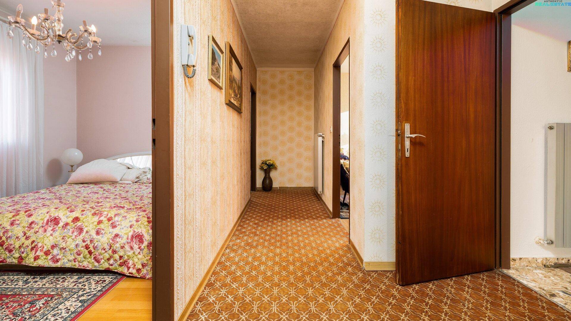 Langer Flur mit gemustertem Teppichboden, Tapeten und Zugang zu verschiedenen Zimmern des Hauses.