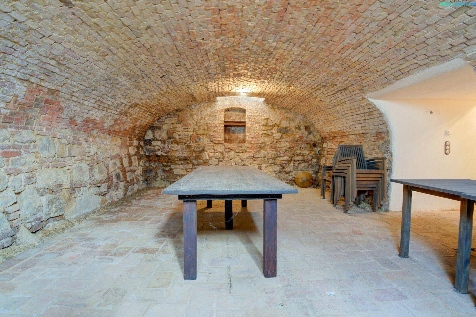 Historischer Gewölbekeller mit Ziegelwänden und Steintischen, ideal für Weinlagerung oder Veranstaltungen.