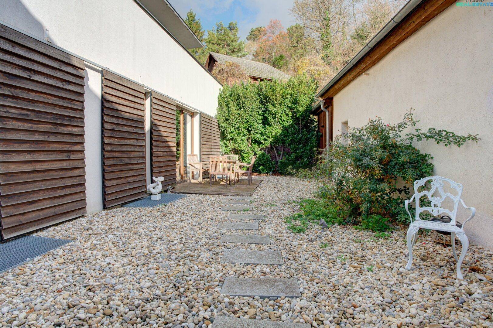 Kleiner Kieshof mit Sitzgelegenheiten und Zugang zu einem Gebäude mit Holzverkleidung.