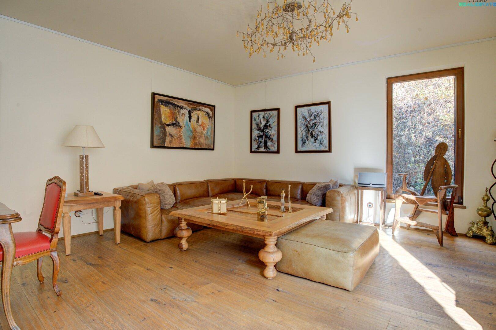 Gemütliches Wohnzimmer mit Ledersofa, Holzboden und großem Fenster, das viel Licht hereinlässt.