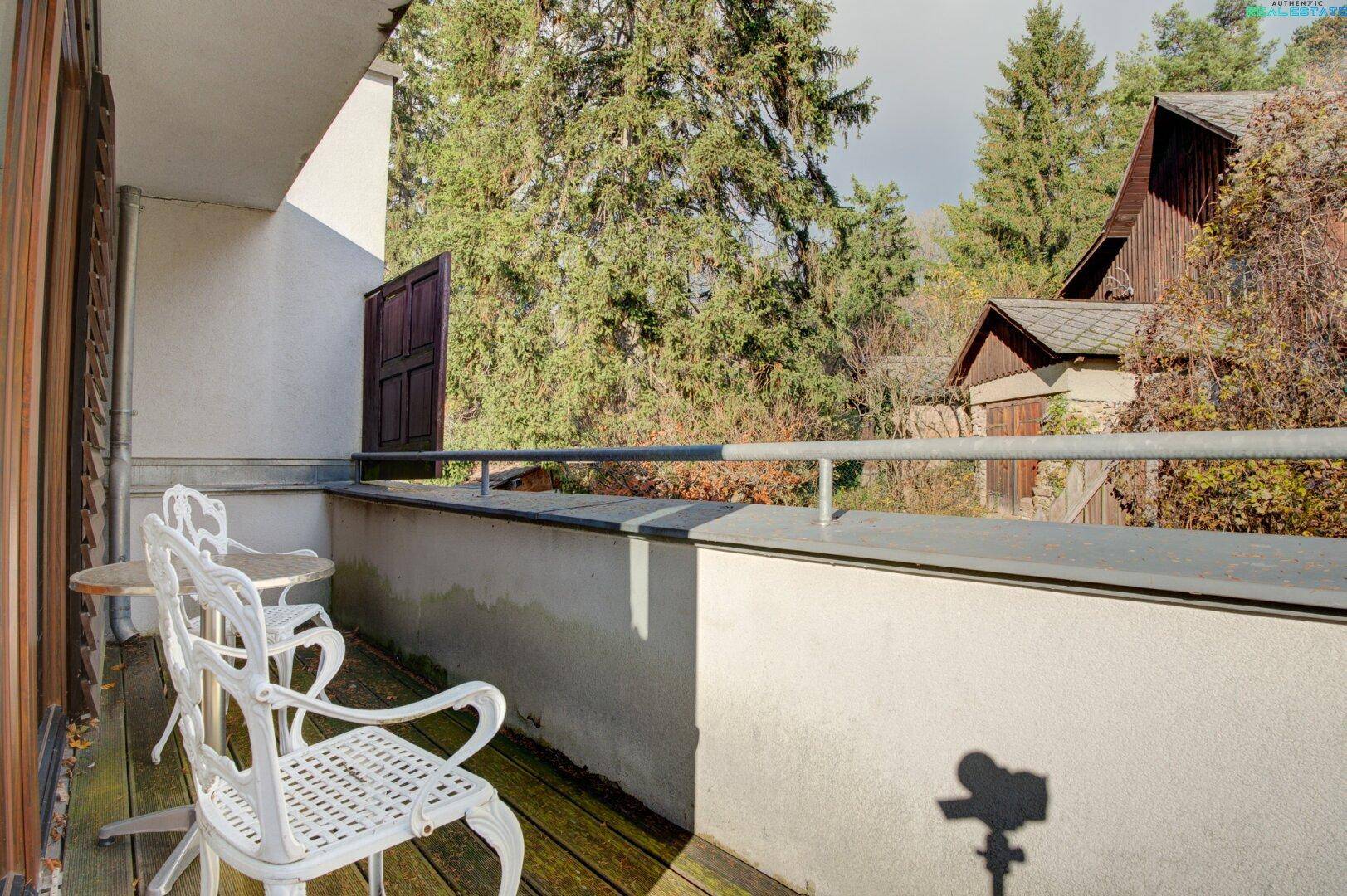 Sonniger Balkon mit Sitzgelegenheiten und Blick auf die bewaldete Umgebung, ideal zum Entspannen.