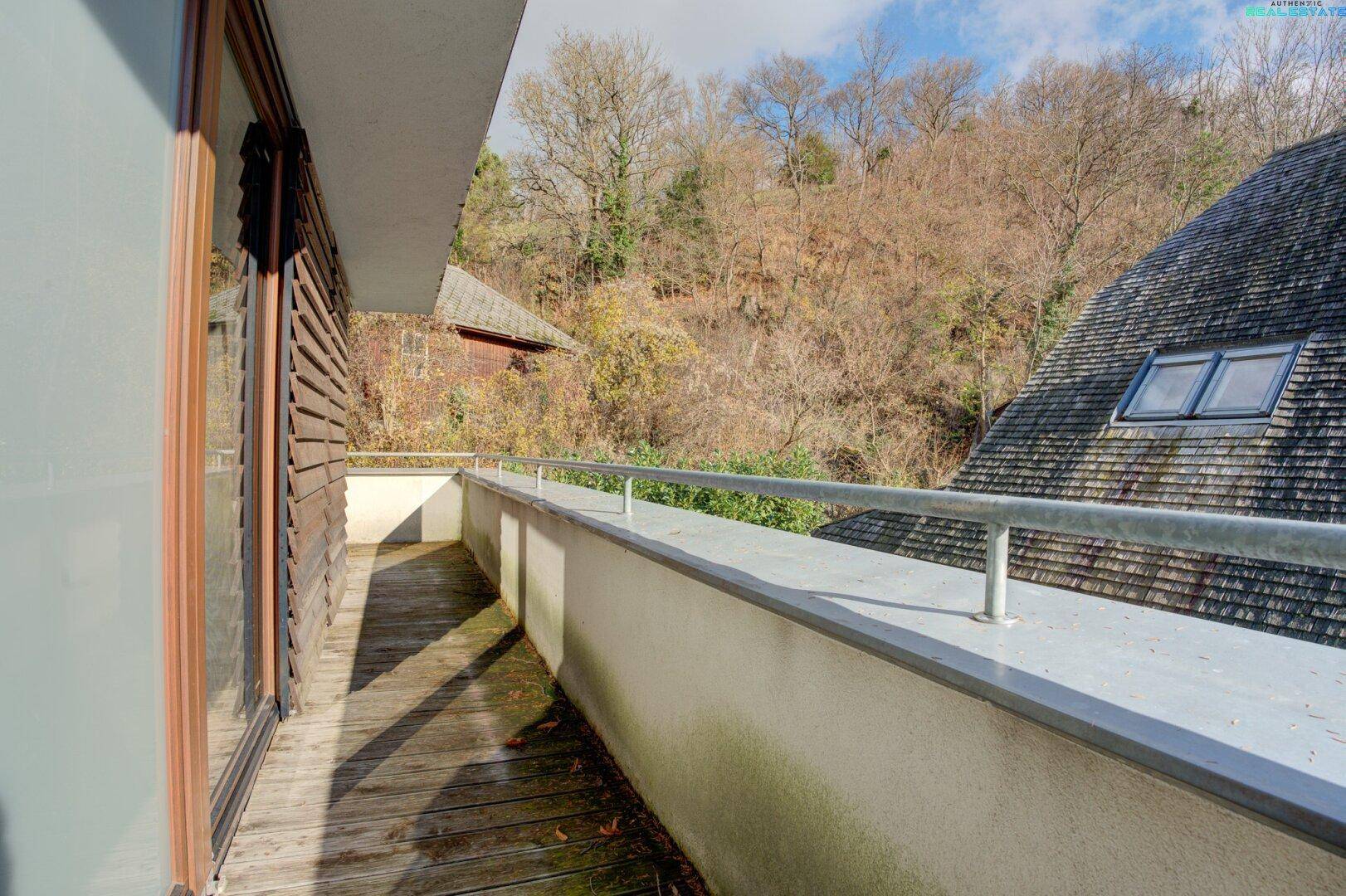 Geräumiger Balkon mit Holzboden und Blick auf die umliegende Natur und Dächer, hell und offen.