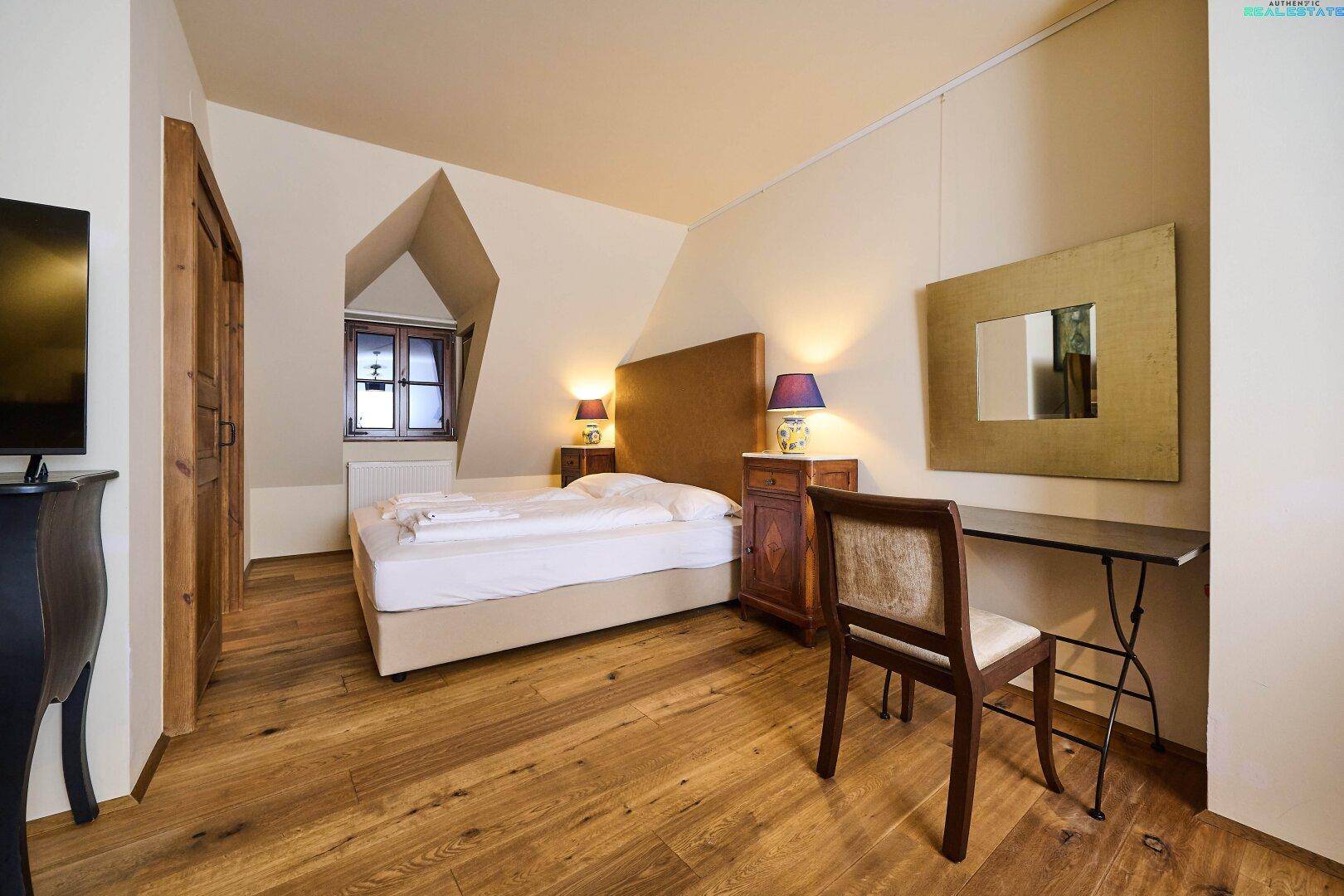 Helles Schlafzimmer in der Dachgeschosswohnung mit Holzboden, Dachfenster und Schreibtischbereich.