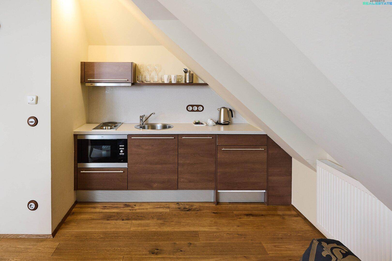 Kompakte Küchenzeile in der Dachgeschosswohnung mit Mikrowelle, Kochfeld und Stauraum unter der Schräge.