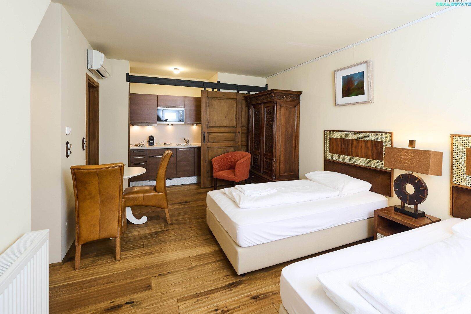 Schlafzimmer in der Dachgeschosswohnung mit zwei Einzelbetten, Holzboden und versteckter Küchenzeile.