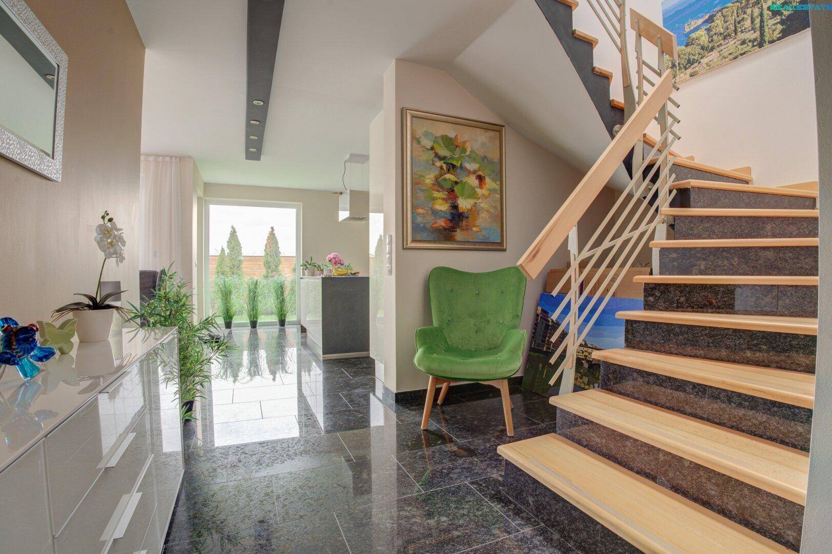 Heller Flur mit Granitboden, Holztreppe und modernem Sessel als Farbakzent.