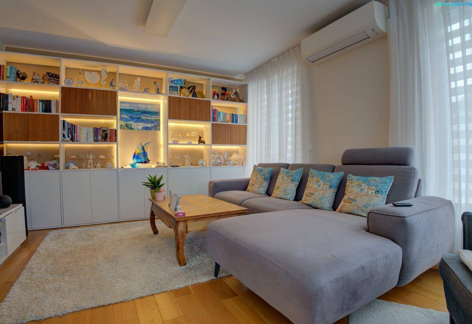 Gemütliches Wohnzimmer mit großem Sofa, beleuchteten Einbauregalen und Holzboden.