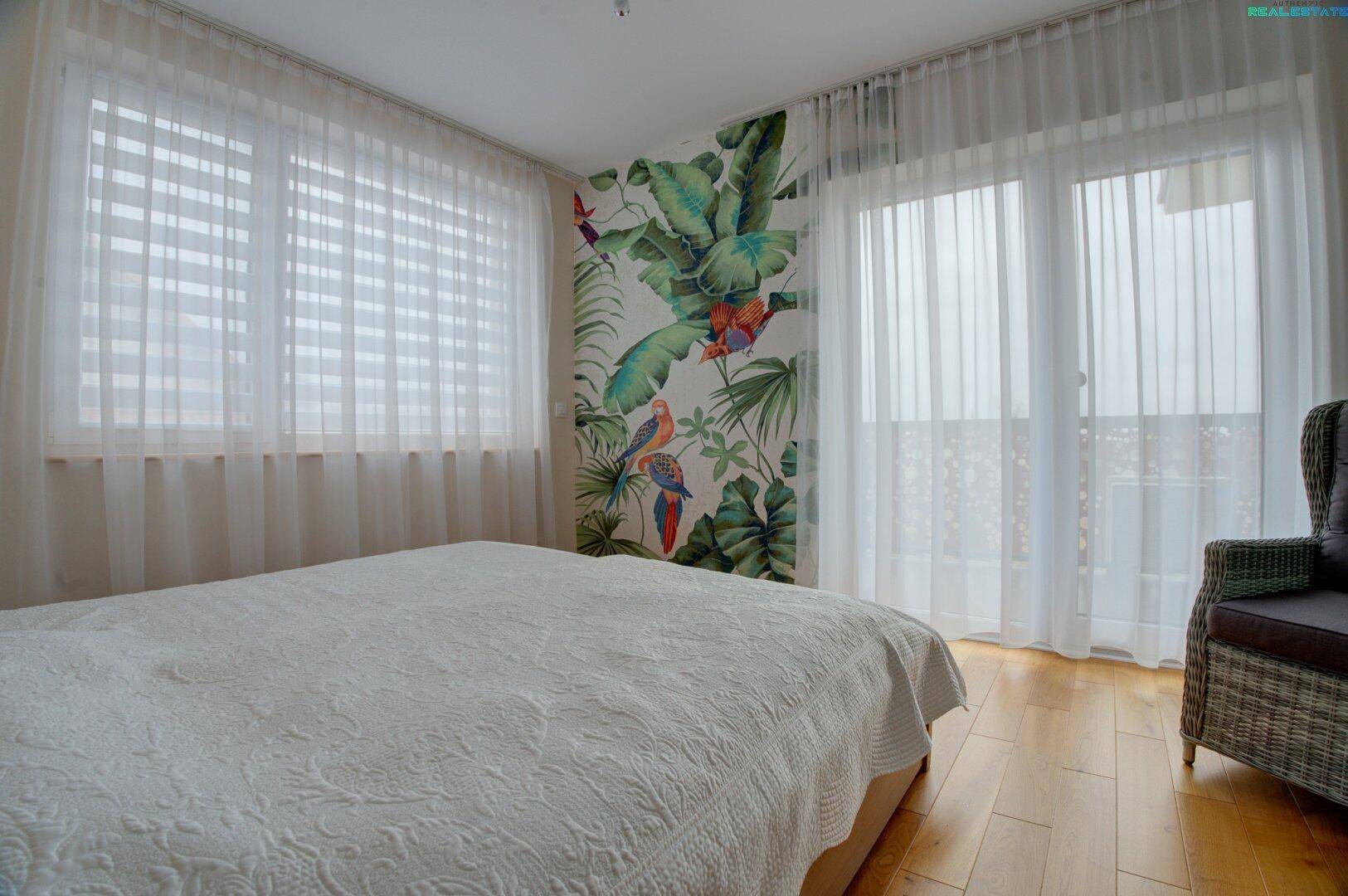 Helles Schlafzimmer mit Holzboden, Doppelbett und Zugang zum Balkon.