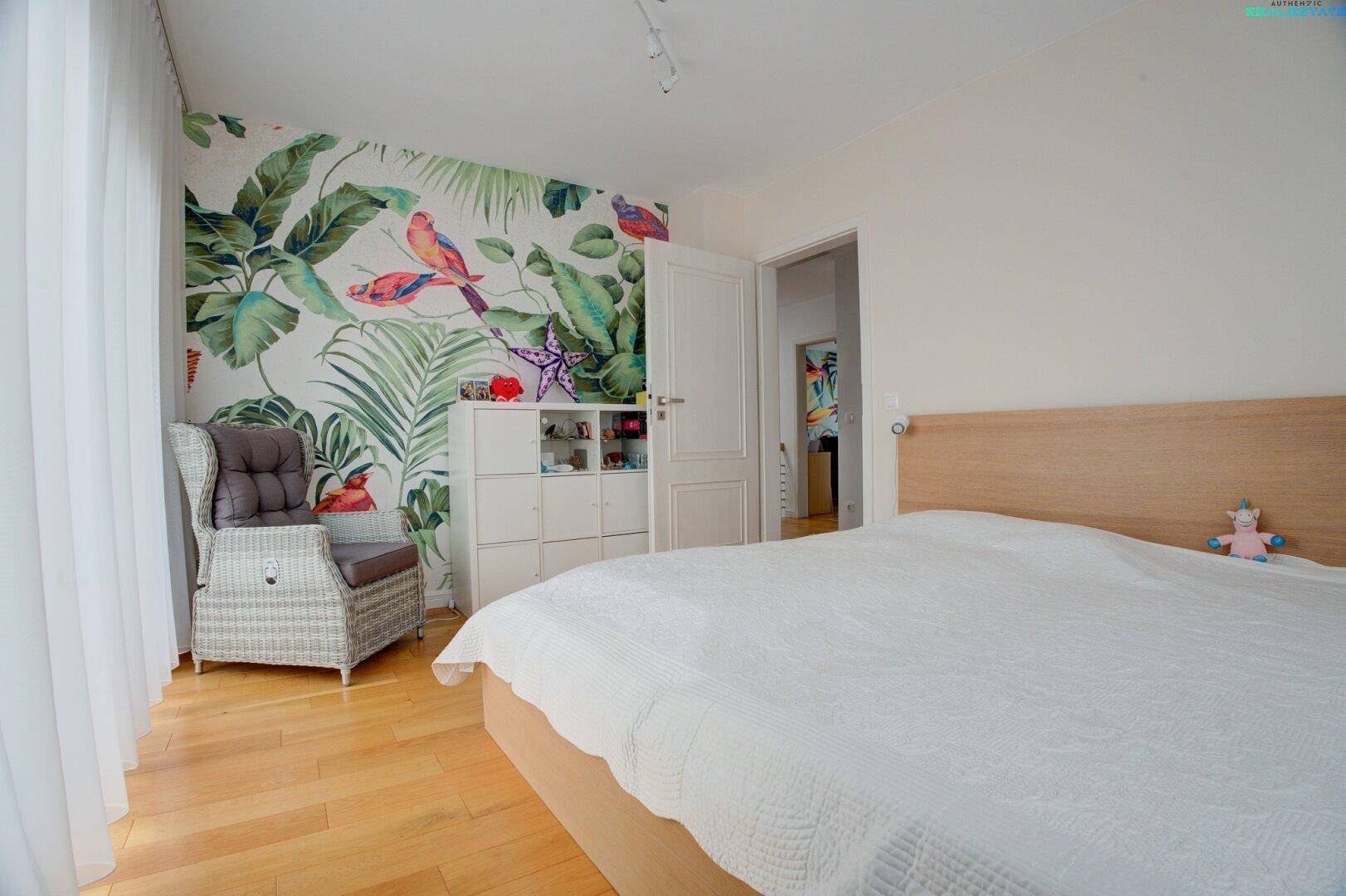 Geräumiges Schlafzimmer mit Holzboden, Doppelbett und farbenfroher tropischer Tapete.