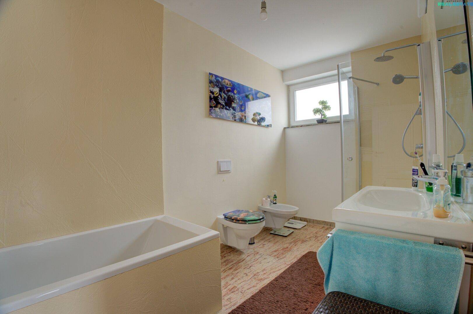 Modernes Badezimmer mit Badewanne, Dusche, Bidet und Fenster für Tageslicht.