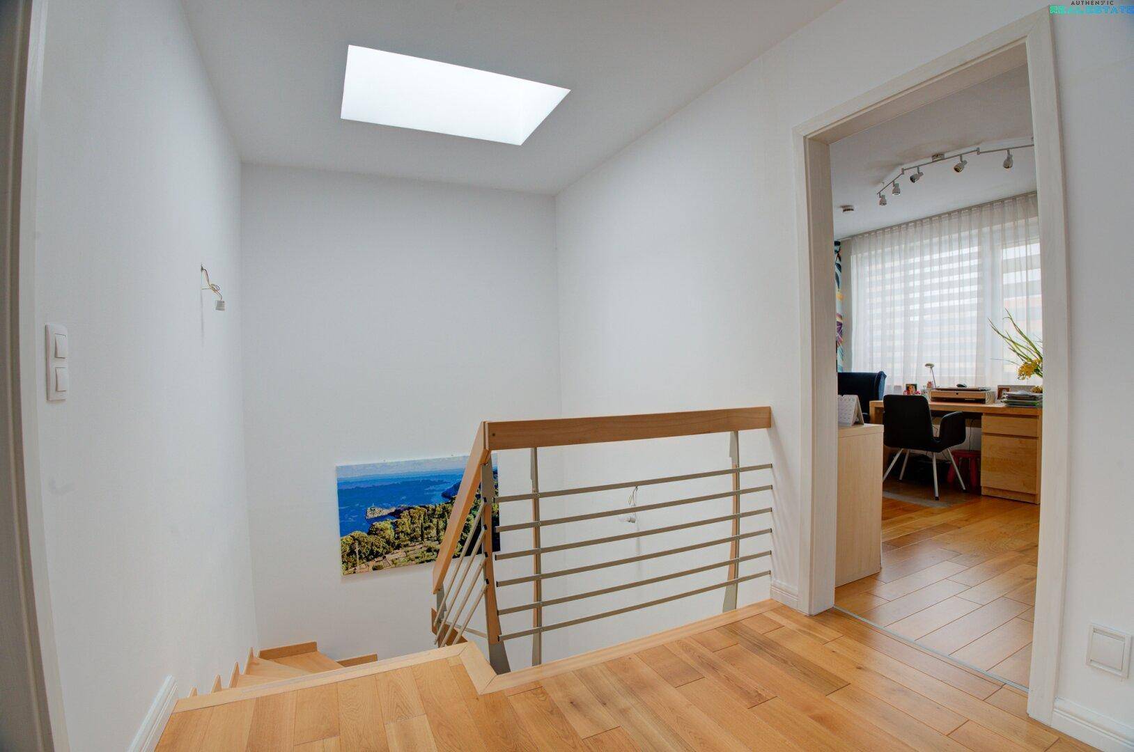 Heller Flur im Obergeschoss mit Holztreppe, weiß gestrichenen Wänden und Oberlicht.