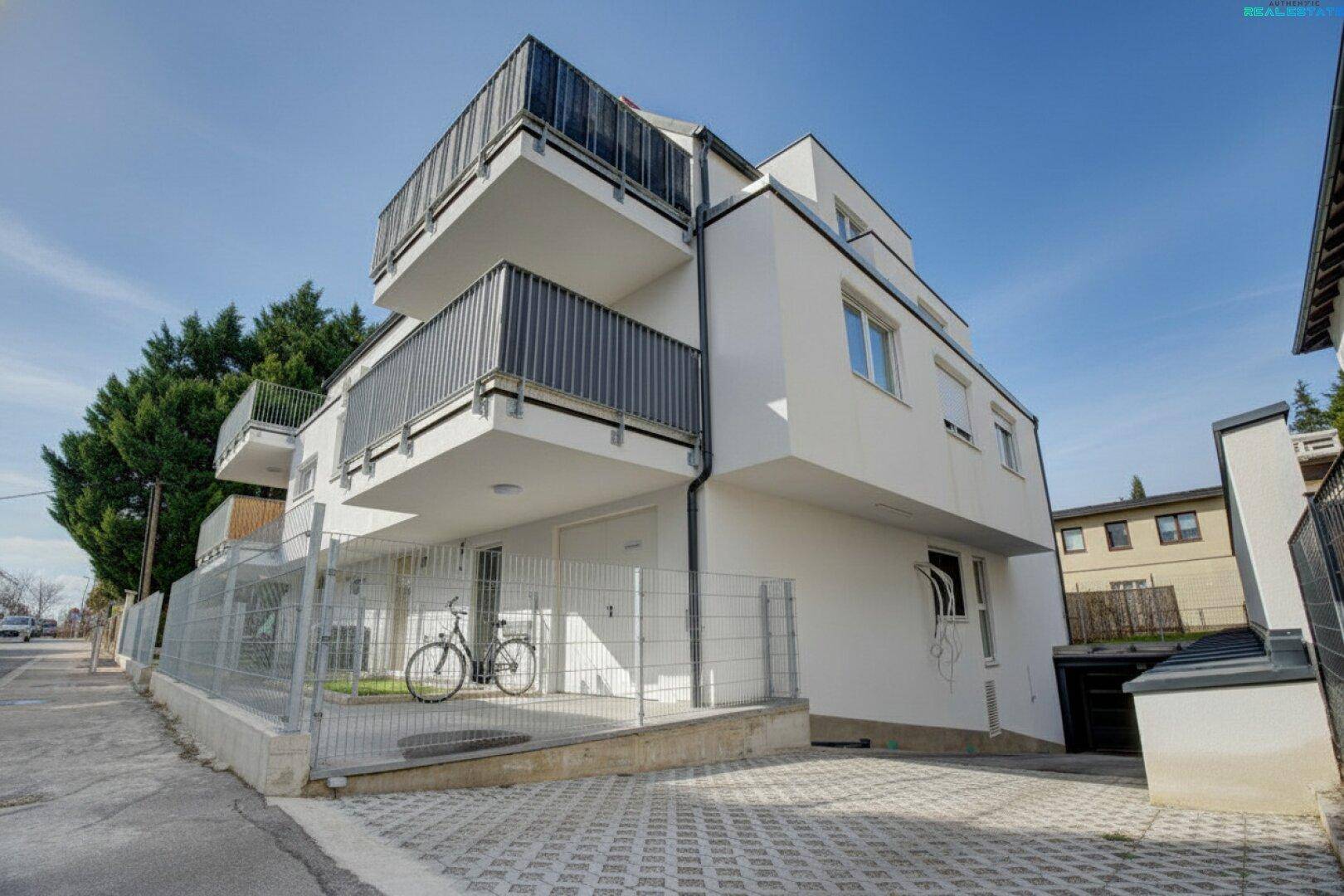 Modernes Mehrfamilienhaus mit weißer Fassade, Balkonen und einem Fahrradabstellplatz im Freien.