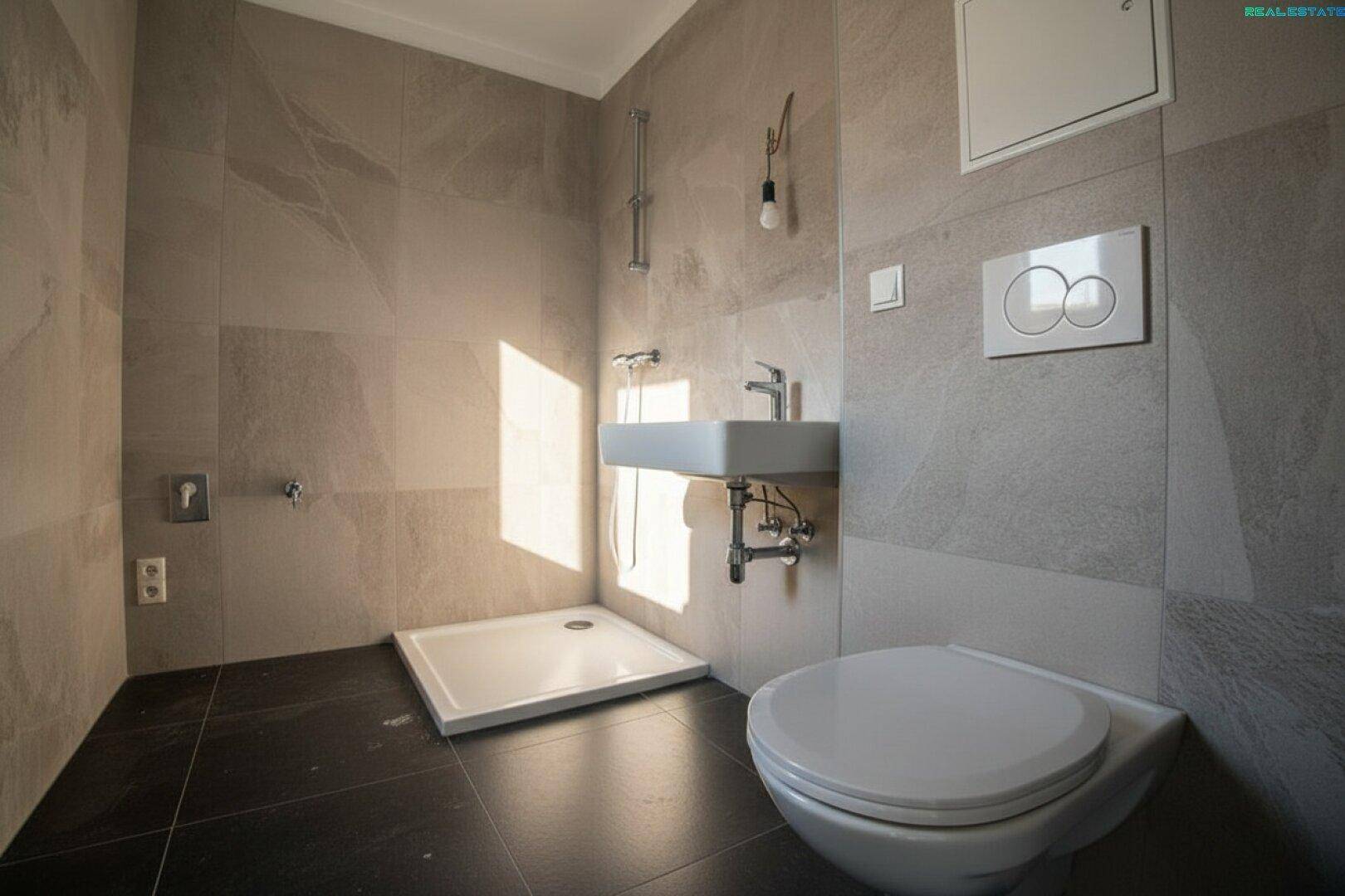 Modernes Badezimmer mit grauen Fliesen, ebenerdiger Dusche und wandhängendem WC.