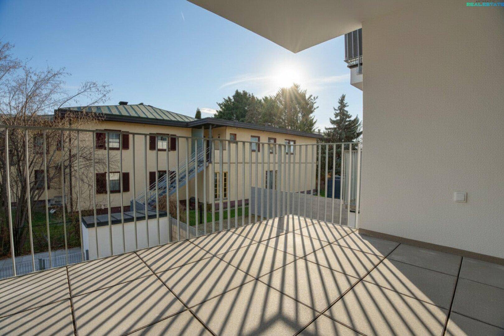 Heller Balkon mit Fliesenboden und Blick auf die umliegenden Gebäude unter strahlendem Sonnenschein.