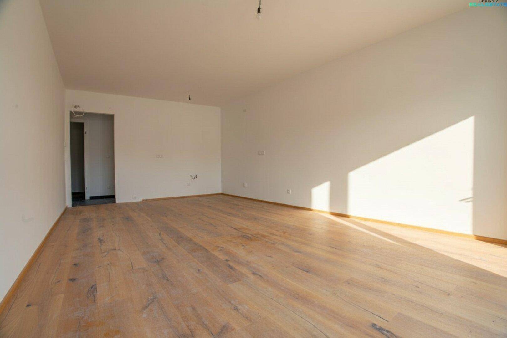 Leerer Wohnbereich mit hellem Holzboden und sonnendurchfluteten Wänden, bereit zur individuellen Gestaltung.