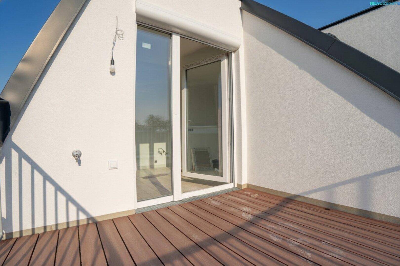 Kleiner Balkon im Dachgeschoss mit Holzboden und Rollladen, zugänglich durch eine große Glastür.