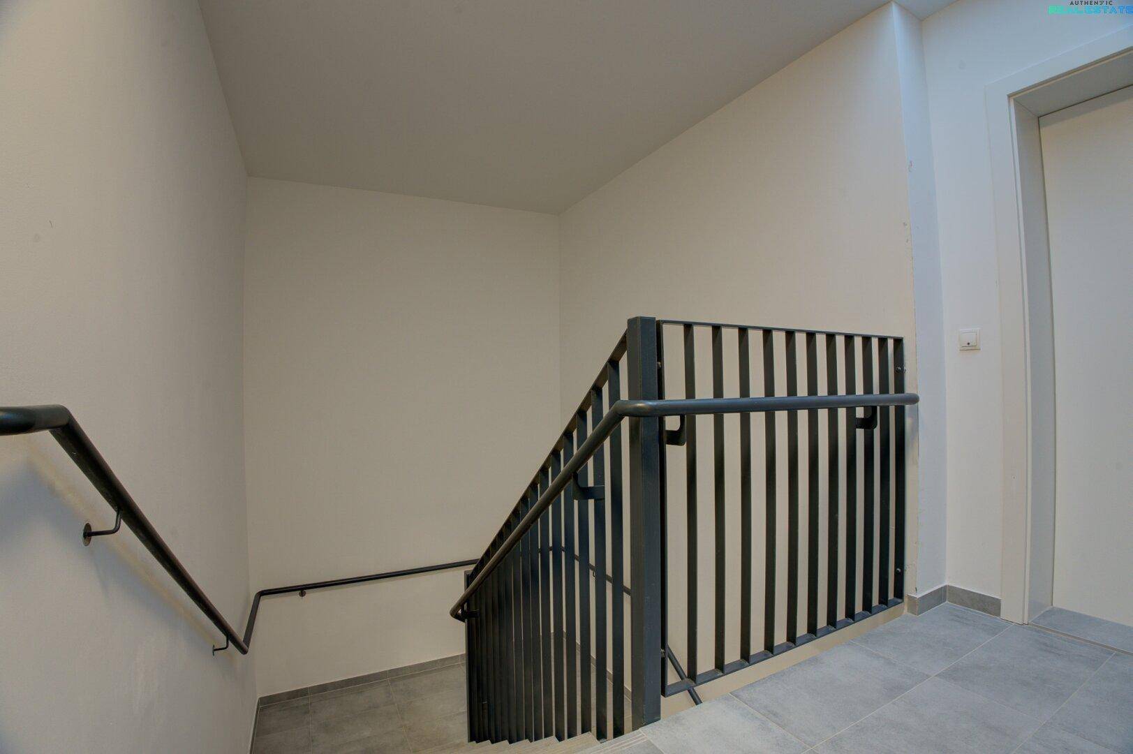 Treppenhaus mit modernem Metallgeländer und Fliesenboden, führt zu den oberen Etagen des Gebäudes.