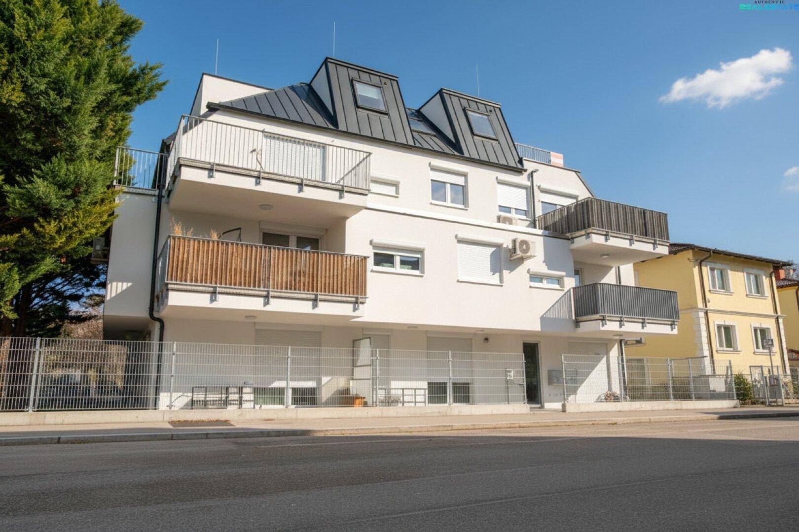 Modernes Mehrfamilienhaus mit weißer Fassade, Balkonen und Dachgauben an einem sonnigen Tag.