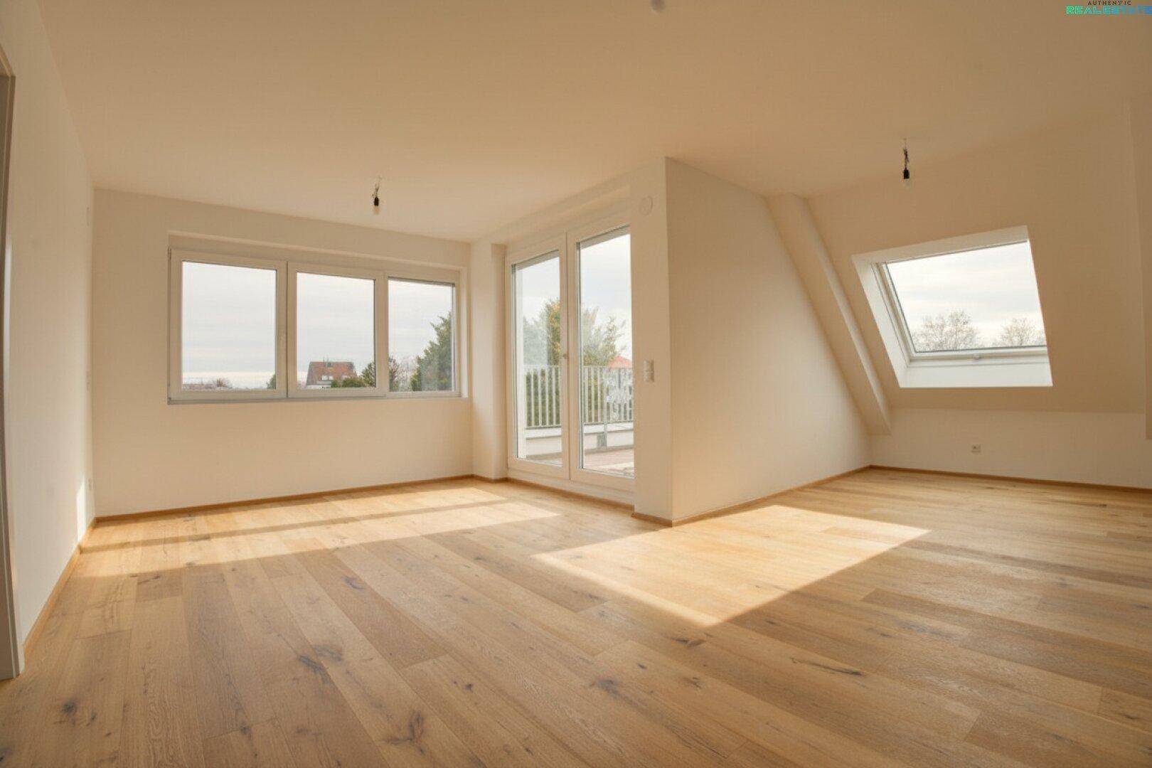 Geräumiges, leeres Wohnzimmer im Dachgeschoss mit Holzboden, großen Fenstern und Balkonzugang.
