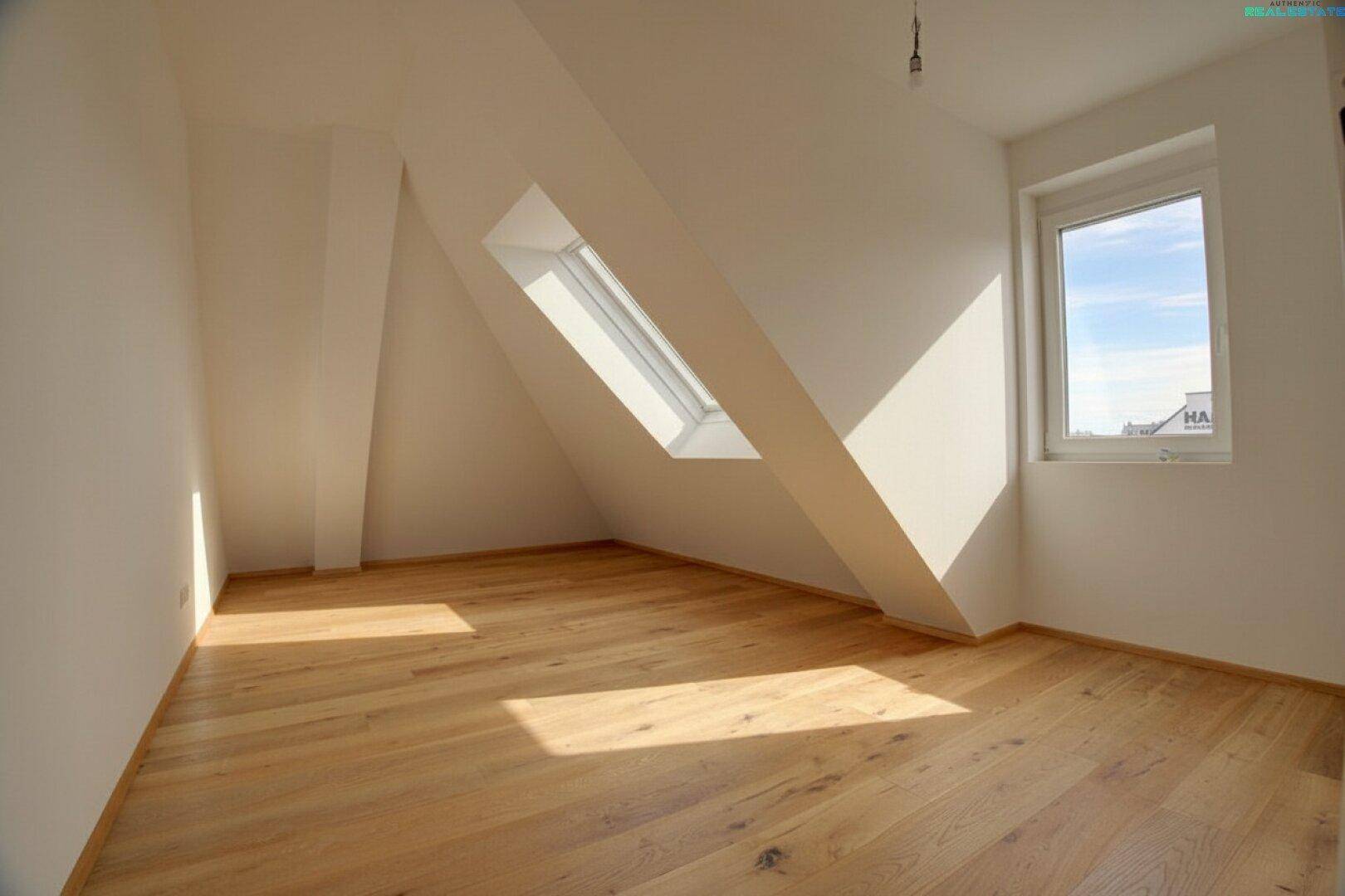 Geräumiges Schlafzimmer im Dachgeschoss mit Holzboden, Dachfenster und einem normalen Fenster.