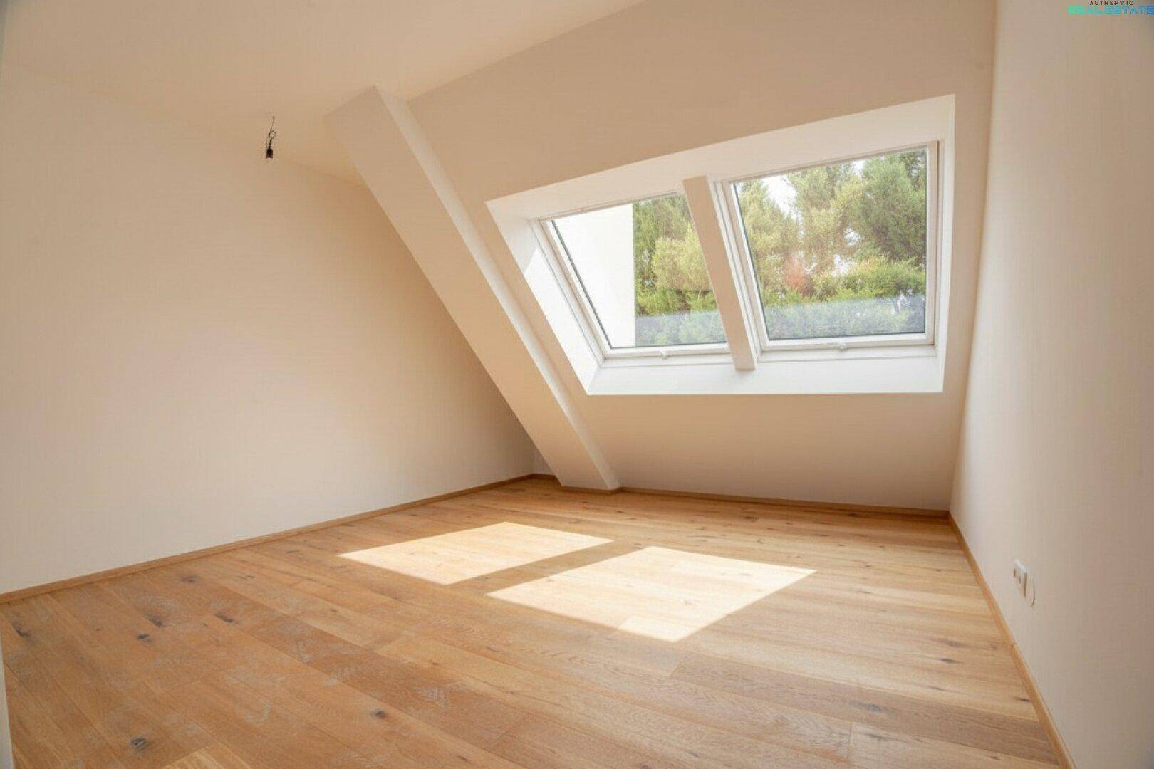 Helles Schlafzimmer im Dachgeschoss mit Holzboden und großen Dachfenstern mit Blick ins Grüne.