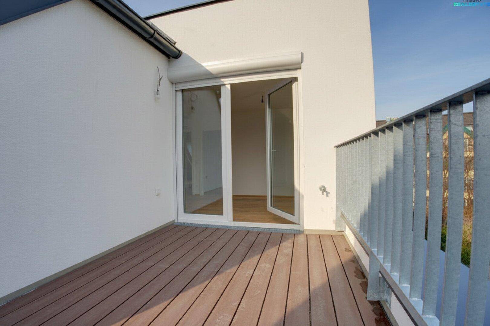 Balkon mit Holzboden und Zugang zum Innenraum durch eine große Glastür mit Rollladen.