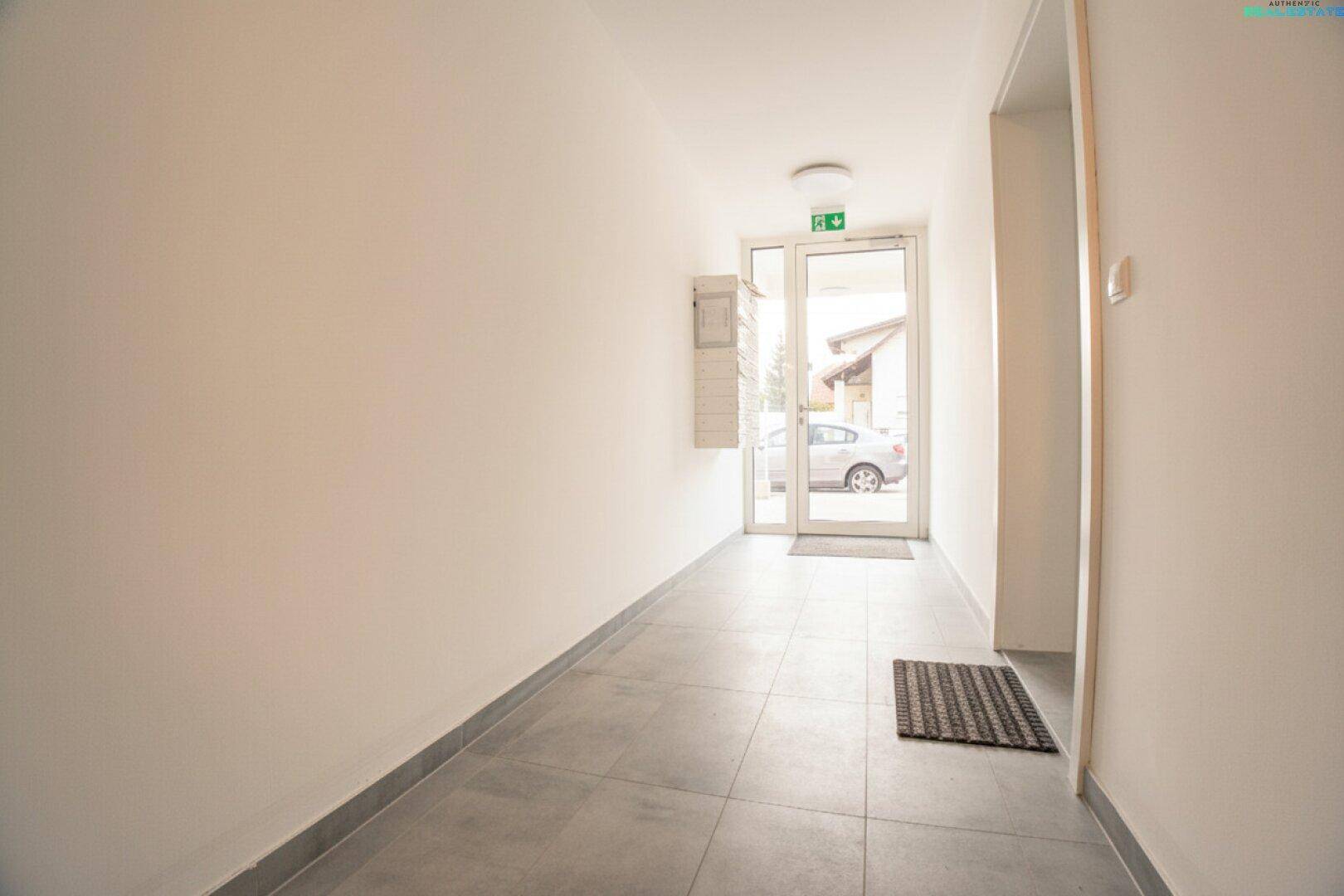 Heller Eingangsbereich mit Fliesenboden und einer Glastür, die Tageslicht hereinlässt.