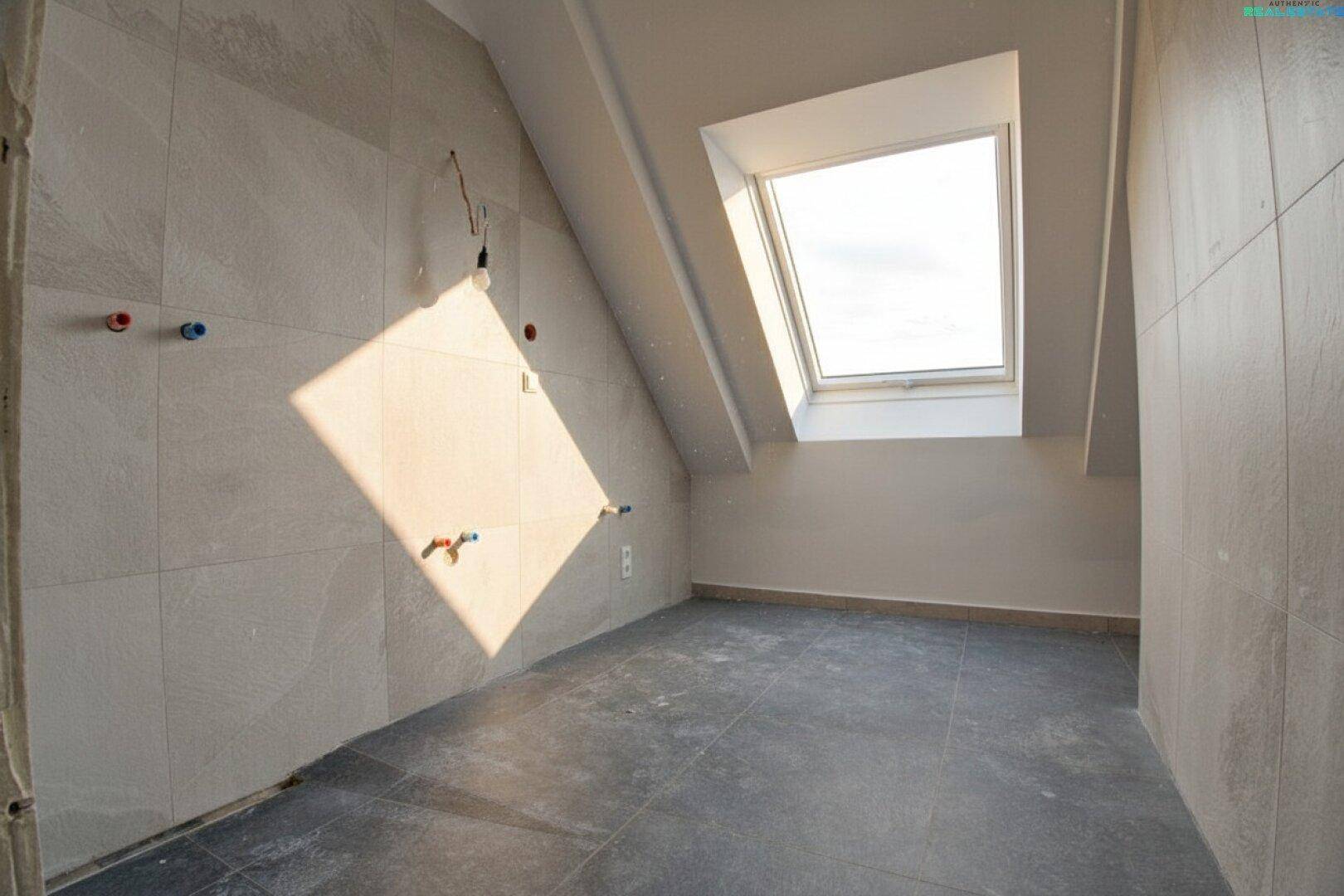 Unfertiges Badezimmer im Dachgeschoss mit Fliesenboden und Dachfenster, bereit für die Installation der Sanitärobjekte.