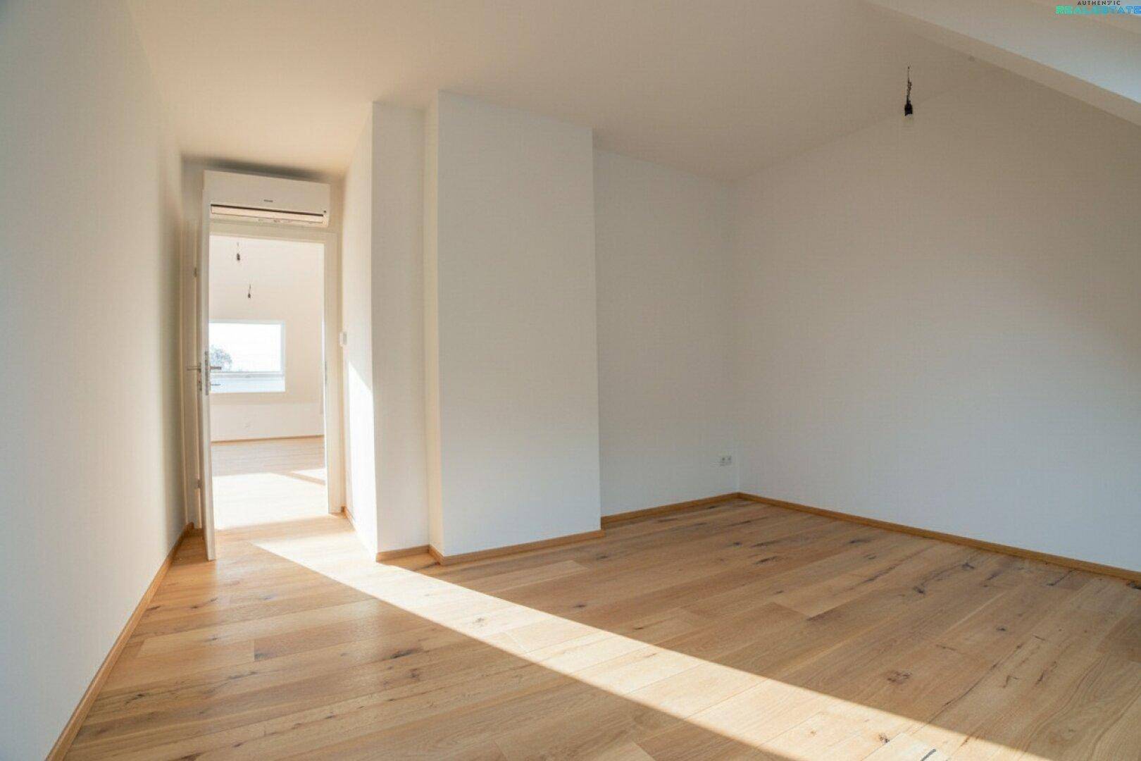 Leeres Schlafzimmer im Dachgeschoss mit Holzboden und Zugang zu einem weiteren Raum.