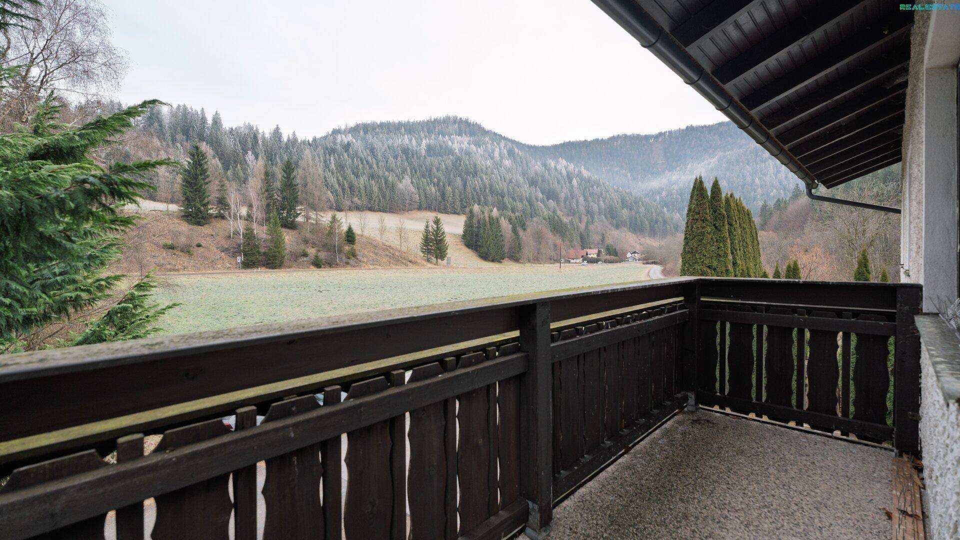 Balkon mit Holzgeländer und weitem Blick über Felder und bewaldete Hügel.