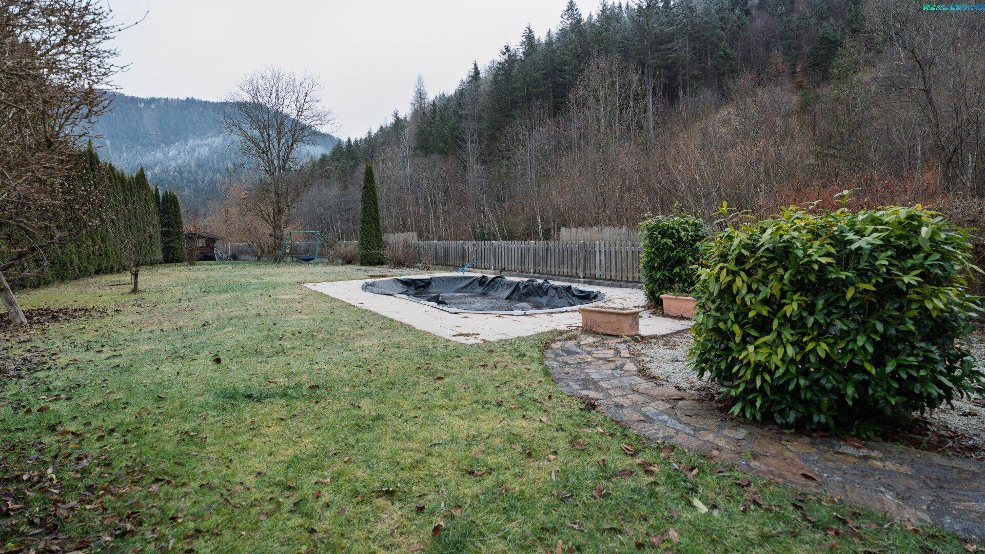 Großer Garten mit Rasenfläche, umzäuntem Poolbereich und Blick auf die bewaldeten Hügel.