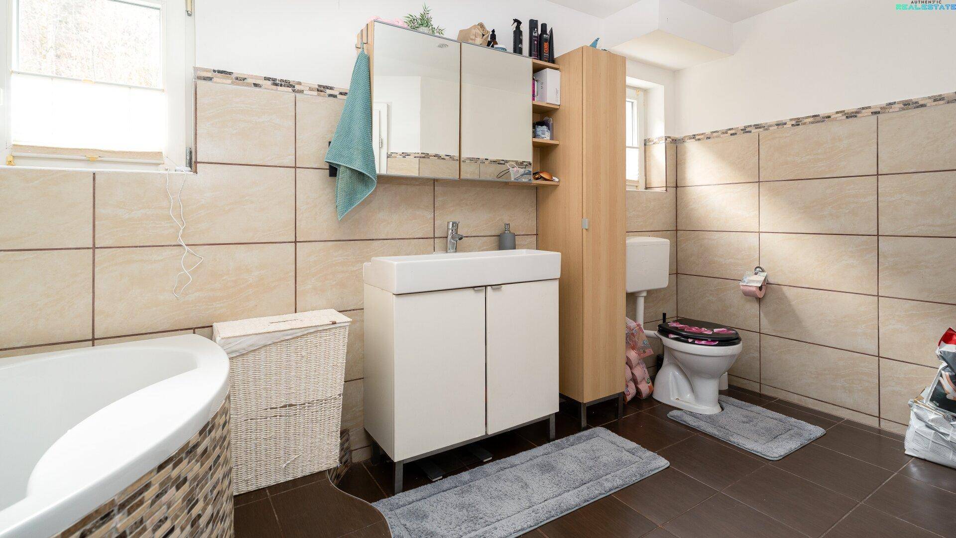 Badezimmer mit WC, Waschbecken, Spiegelschrank und beigen Wandfliesen.