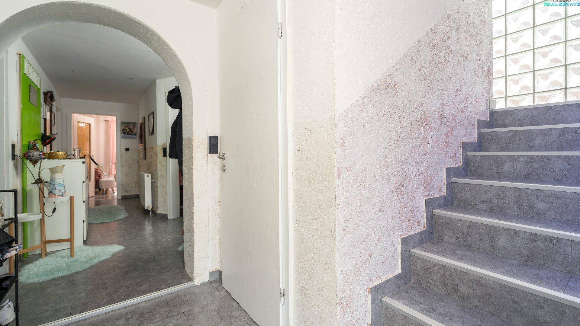 Eingangsbereich mit Treppe und einem Bogen, der zu weiteren Räumen führt.