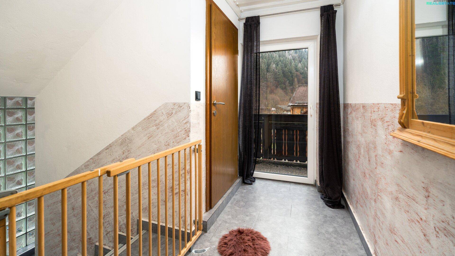 Treppenabsatz mit Zugang zu einem Balkon und Blick auf die bewaldete Umgebung.