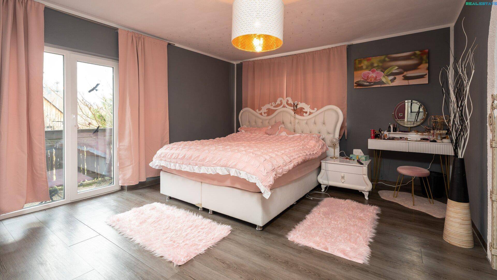 Schlafzimmer mit großem Bett, rosa Dekoration und Zugang zu einem Balkon.